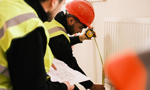 Workers measuring radiator against plans