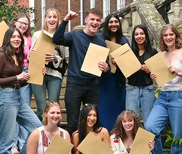 A group of students all cheering and holding brown envelopes with their results in them