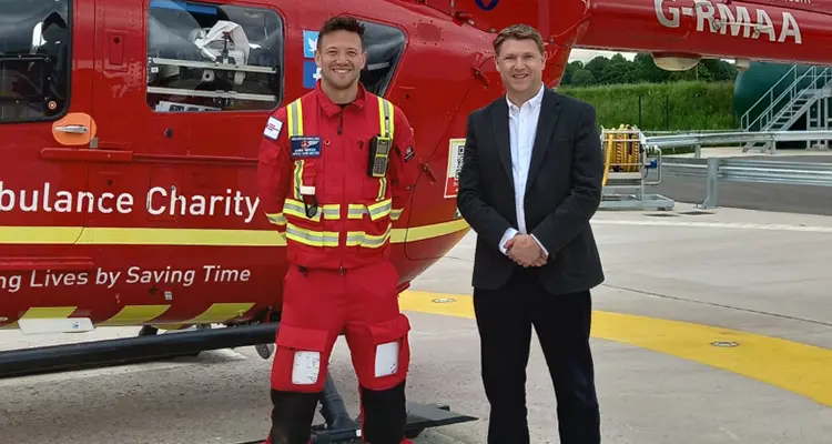 College principal and midlands air ambulance representative standing in front of helicopter smiling