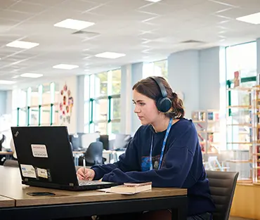 Close up of female student working in library on laptop