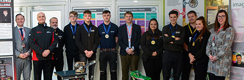 A group of apprentices, College staff, including the Principal and employers standing behind two robots 