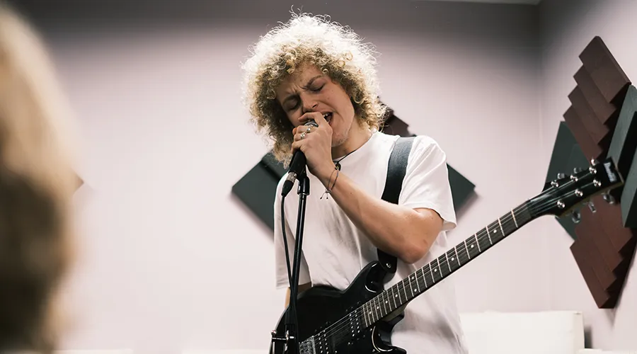 Student with guitar singing into microphone