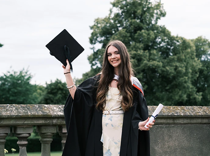 Young student wearing gown and holding cap outside